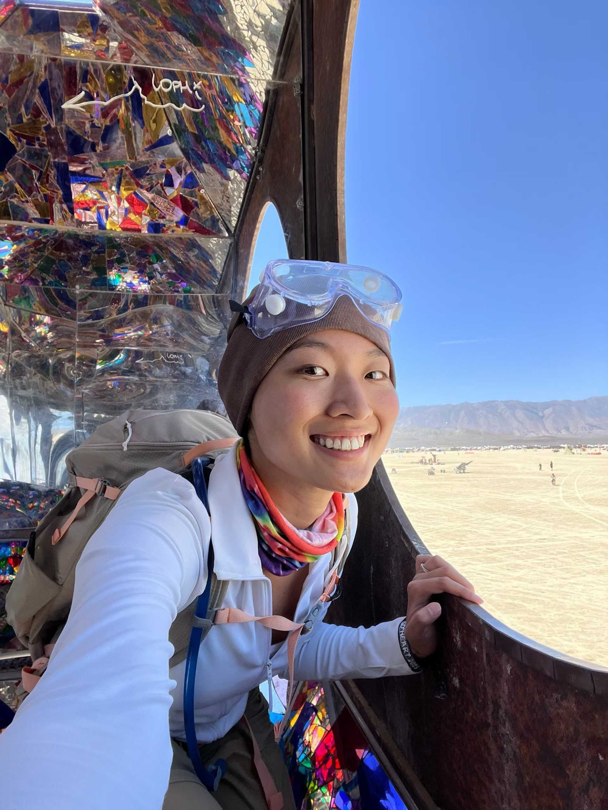 Fuma at Black Rock City with goggles and a desert camp behind her