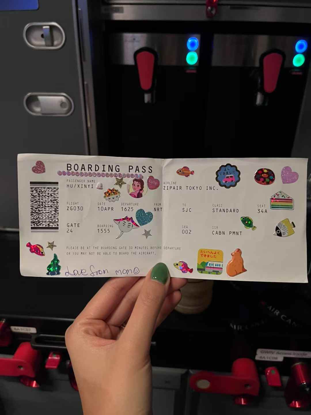 A boarding pass covered in colorful stickers held inside an airplane galley